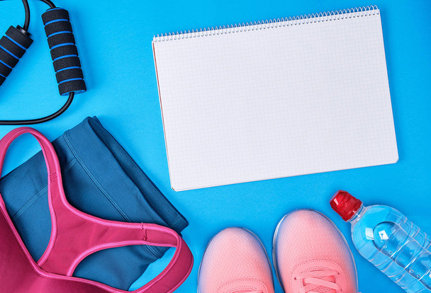open notebook with blank white sheets, sportswear, sporty blue background, top view - Φωτογραφία, εικόνα