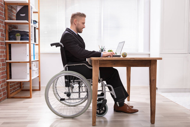 Disabled Businessman Sitting On Wheelchair Using Laptop At Workplace - Foto, Bild