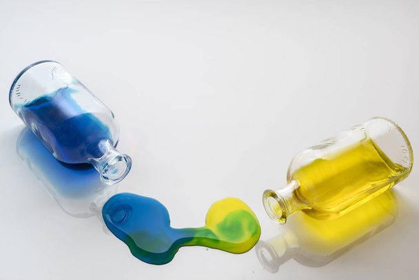 colored liquid spill by a small glass bottle on a white surface - Foto, immagini