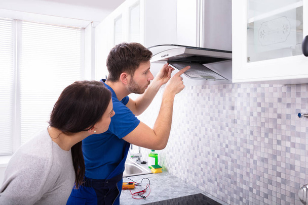 Pretty Young Woman Looking At Repairman Fixing Kitchen Extractor Filter Over Kitchen Counter - Foto, Imagem