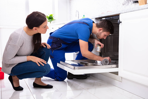 Young Woman Looking At Repairman Repairing Dishwasher In Kitchen - Foto, imagen