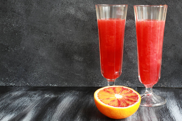 Freshly squeezed blood orange juice with orange fruit in shabby looking glasses on dark board - Foto, afbeelding