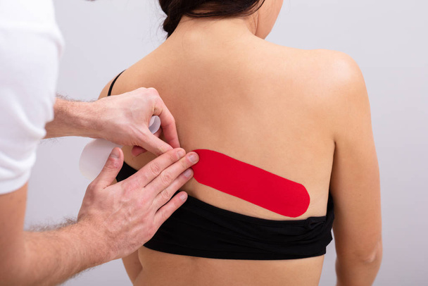 Close-up Of Man Hand's Applying Red Physio Tape On Woman's Back - 写真・画像