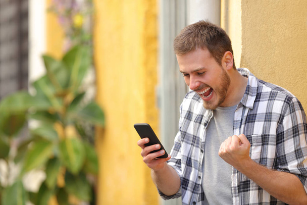 Excited man in the street checking smart phone celebrating good news - Фото, изображение