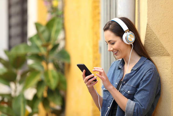 Happy girl listening to music downloading songs leaning on a colorful wall in the street - 写真・画像