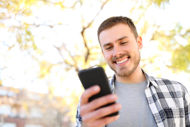 Счастливчик использует смартфон в парке с деревьями на заднем плане
 - Фото, изображение