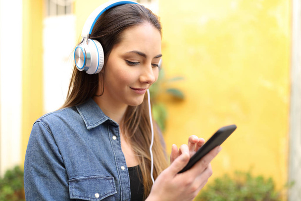 Serious woman listening to music using smart phone searching songs in the street - Foto, Imagen