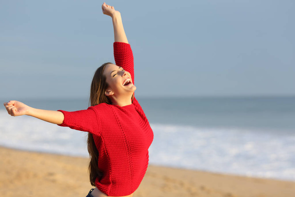Excited girl in red celebrating vacation on a beach raising arms - Foto, imagen