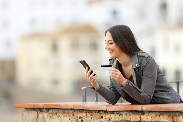 Happy online buyer paying with smart phone and credit card in a rural apartment balcony - Foto, Bild