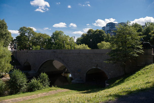 schöne alte Brücke über den Fluss, grüne Pflanzen und moderne Gebäude im Hintergrund in Oslo, Norwegen  - Foto, Bild