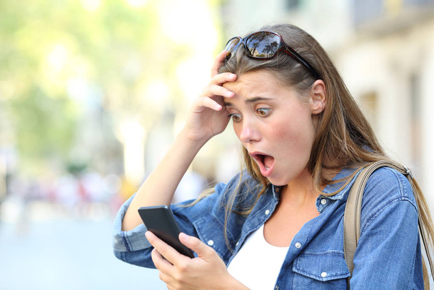 Shocked teenage girl checking smart phone discovering mistake content in the street - Fotó, kép