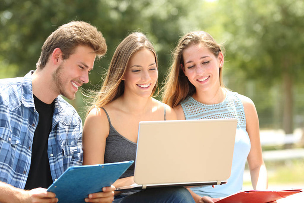 Three happy students e-learning together sitting on a bench in a campus - Foto, Imagen
