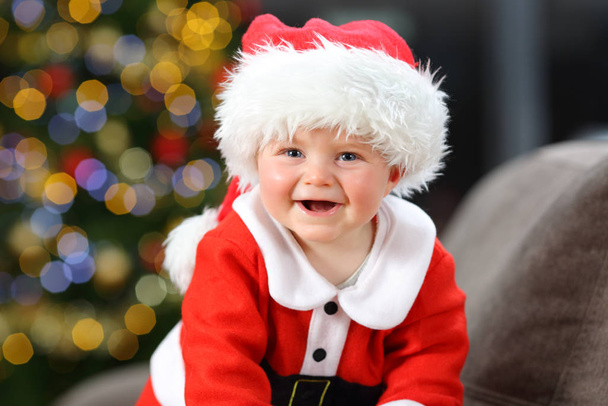 Baby wearing santa claus disguise looking at camera in christmas on a couch in the living room at home - Photo, Image