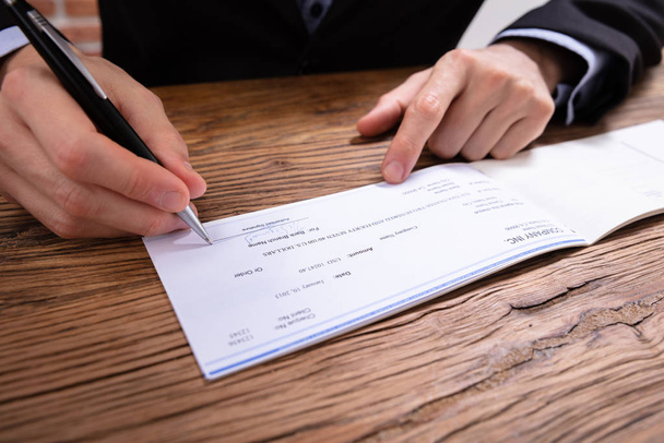 Close-up Of A Businessperson's Hand Signing Cheque With Pen In Office - Фото, изображение