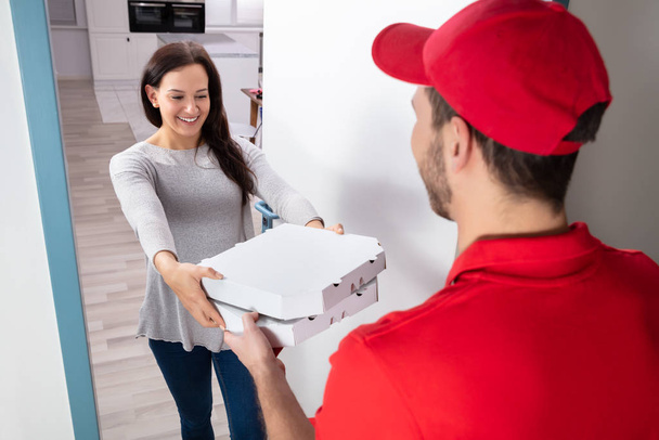 Smiling Woman Receiving Pizza From Delivery Man At Home - Фото, изображение