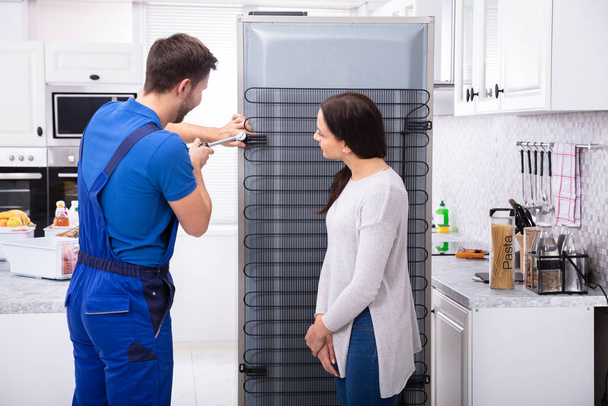 Woman Looking At Technician Repairing Refrigerator With Screwdriver In Kitchen - Zdjęcie, obraz