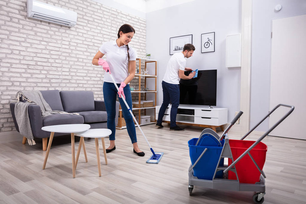 Giovani lavoratori pulizia televisione e pavimento con scopa e spugna a casa
 - Foto, immagini