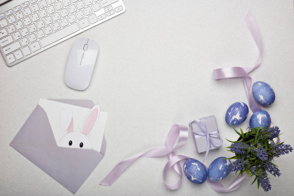 Colored easter eggs, gift box, computer keyboard and mouse, blank sheet with envelope on a lilac  background. Top view with copy space. Greeting card, Easter background - Фото, изображение