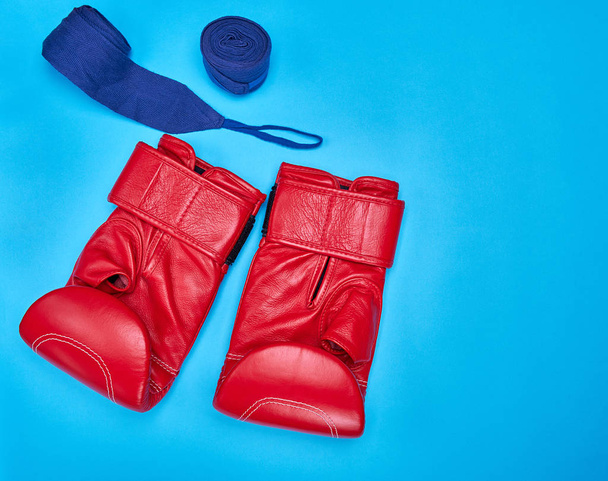 a pair of red leather boxing gloves and a textile bandage on a blue background, copy space - 写真・画像