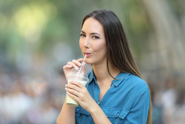 Happy woman drinking milk shake with a straw in the street looking at you - Foto, afbeelding
