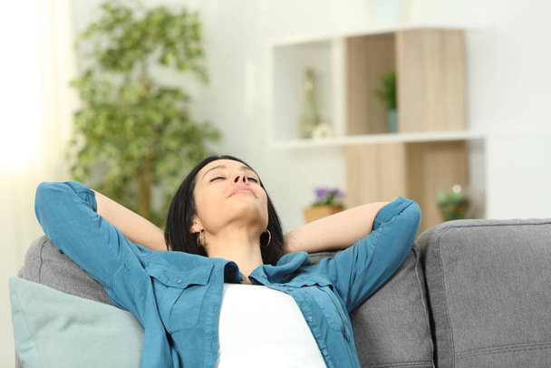 Relaxed woman resting with arms on head sitting on a sofa at home - Photo, Image