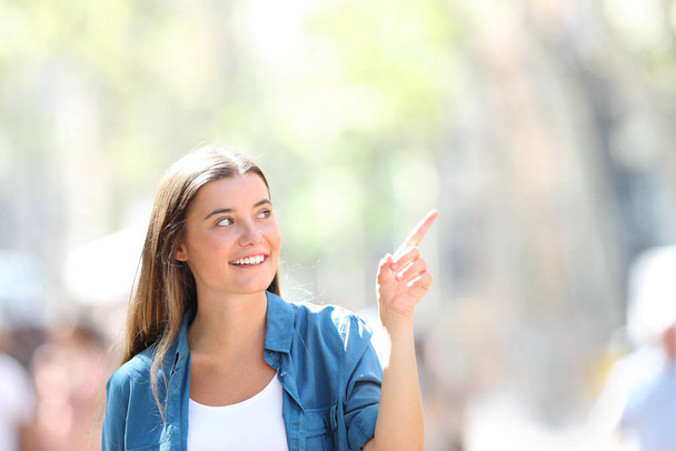 Frint view portrait of a happy girl pointing at side in the street a sunny day - Foto, Imagen
