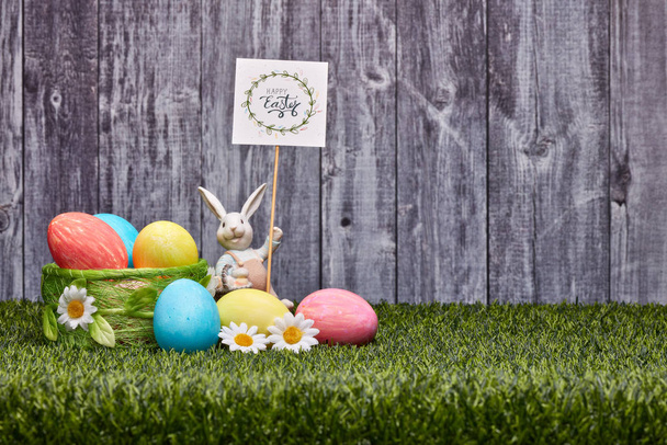 Colored easter eggs, easter rabbit and flowers lying on a green grass on a grey wooden  background with copy space. Greeting card, Easter background - Fotoğraf, Görsel