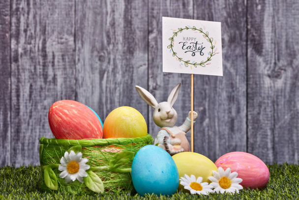 Colored easter eggs, easter rabbit and flowers lying on a green grass on a grey wooden  background with copy space. Greeting card, Easter background - Φωτογραφία, εικόνα