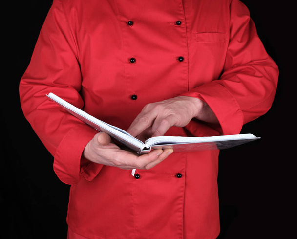 chef in red uniform holding open notepad , black background - Fotoğraf, Görsel
