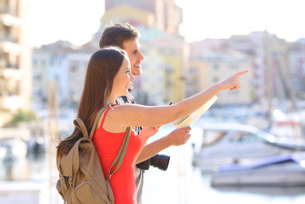 Happy couple of tourists pointing landmarks on vacation in a coast town - Valokuva, kuva