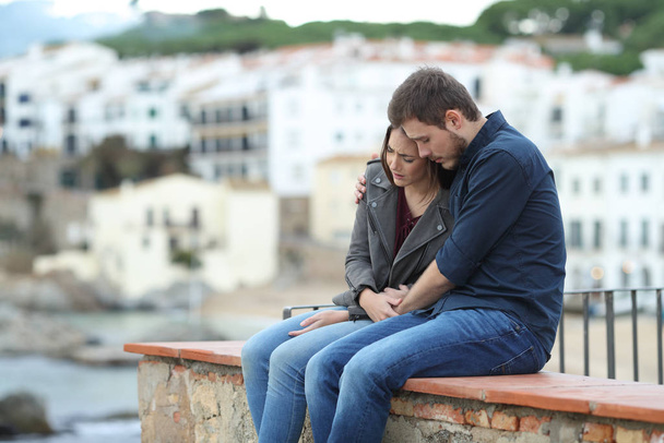 Sad woman and man comforting her on a ledge with a town in the background - Фото, зображення