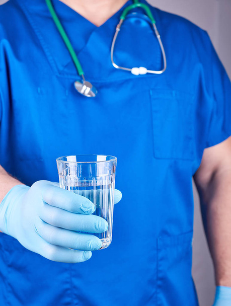 doctor in blue uniform and latex gloves holding a glass of water, selective focus - Φωτογραφία, εικόνα