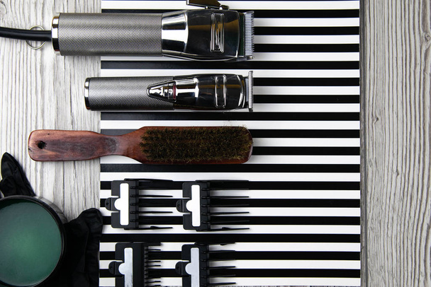 Máquinas de corte de cabelo, bicos de diferentes tamanhos, pentes e géis para styling, dispostos em um belo listrado branco preto
 - Foto, Imagem