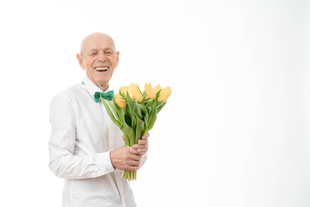 Happy, glad, cheerful, joyful smiling old man in white shirt, senior holds bouquet of yellow flowers in hands and looking at the camera isolated over white background, copyspace for your text - Women - Fotografie, Obrázek