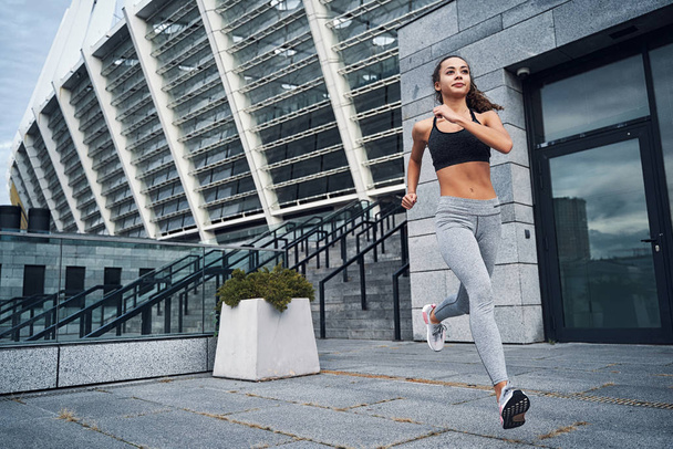 Młoda atletyczna kobieta biegnąca na stadionie miejskim z tłem miejskich schodów - Zdjęcie, obraz