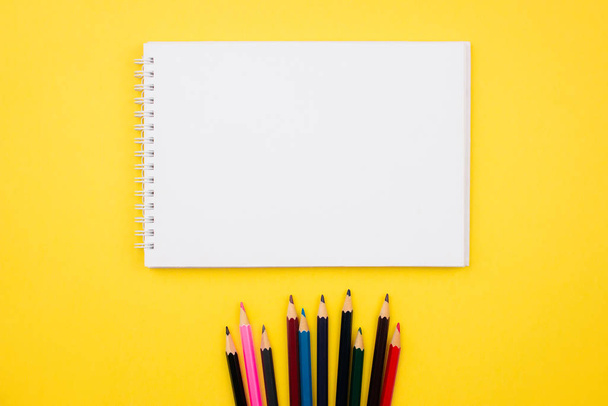 Sketchbook, notebook and color pencils flat lay on colorful yellow background. Top view with copy space. School and office supplies layout. Back to school concept. Template for web. Stock photo. - 写真・画像