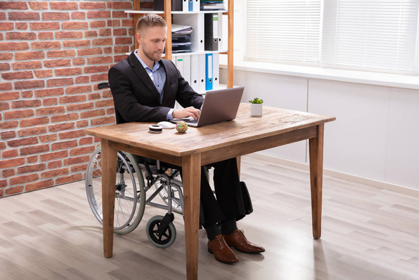 Disabled Businessman Sitting On Wheelchair Using Laptop At Workplace - Fotoğraf, Görsel