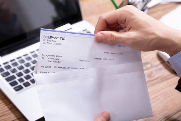 Close-up Of A Businessperson's Hand Opening Envelope With Paycheck Over Wooden Desk - Photo, Image