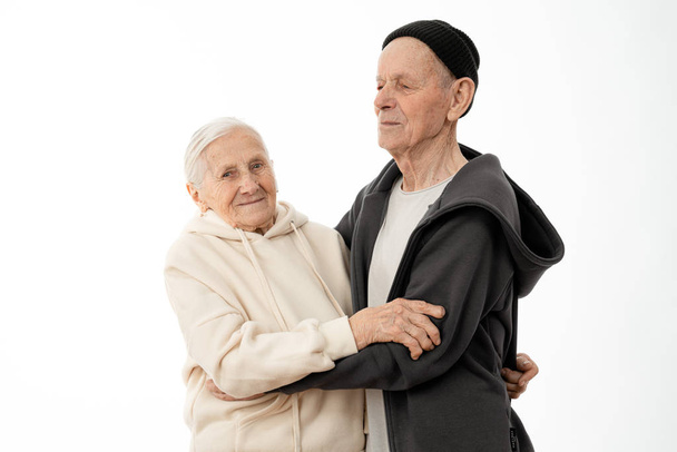 Attractive lovely old seniors couple in hoodies dancing isolated over white background - Foto, imagen