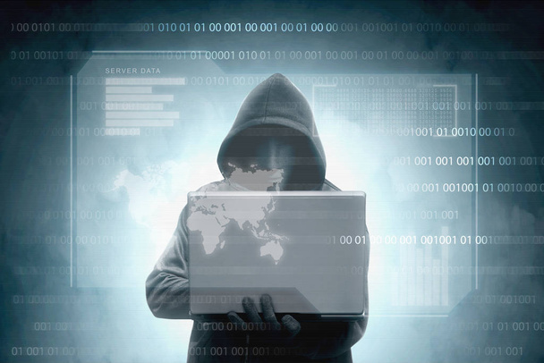 Hacker in black hoodie holding laptop with virtual display server data, chart bar, binary code and world map over dark background - Fotografie, Obrázek