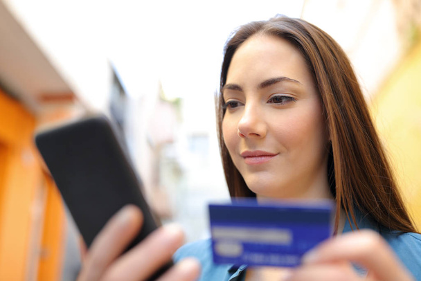 Femme sérieuse payer avec carte de crédit et téléphone intelligent à l'extérieur dans la rue
 - Photo, image