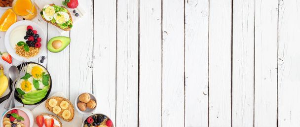 Healthy breakfast food banner with side border. Table scene with fruit, yogurt, smoothie, nutritious toasts and egg skillet. Top view over a white wood background. Copy space. - Photo, Image