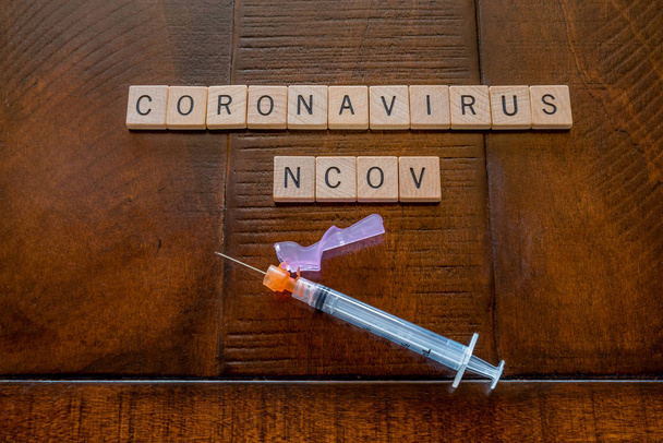 Coronavirus NCOV palabras hechas de baldosas de madera con una jeringa sobre un fondo de madera: salud y concepto médico
 - Foto, Imagen