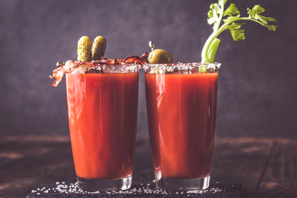 Two glasses of Bloody Mary garnished with gherkins and celery stalk - Foto, Bild