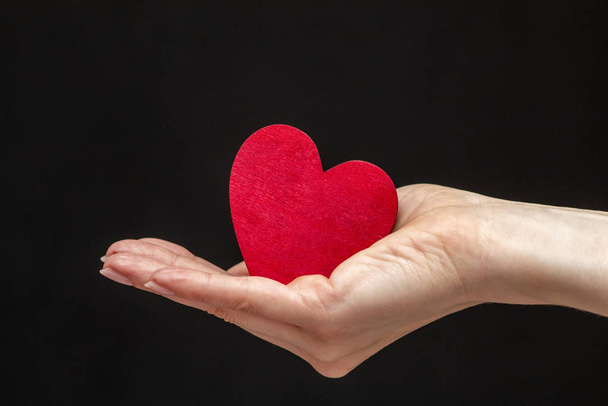 человек держит в руках красное сердце на чёрном фоне
 - Фото, изображение