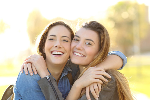 Портрет счастливых друзей с идеальной улыбкой, обнимающихся, смотрящих на тебя в парке на закате
 - Фото, изображение