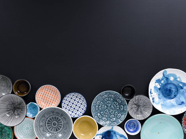 white and coloured tableware in different designs on a black background, photographed from above - Foto, immagini