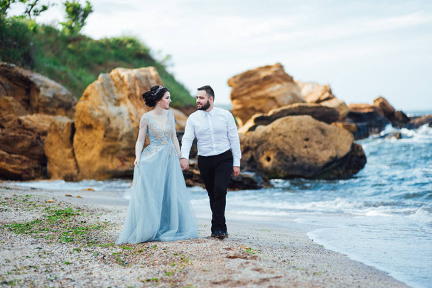 same couple with a bride in a blue dress walk along the ocean shore - Foto, Imagen