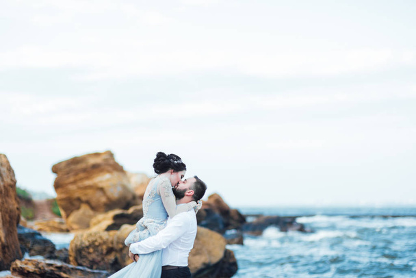 same couple with a bride in a blue dress walk along the ocean shore - Фото, зображення