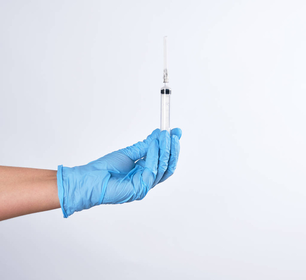 hand in a blue sterile glove holds a plastic syringe on a white background - Zdjęcie, obraz
